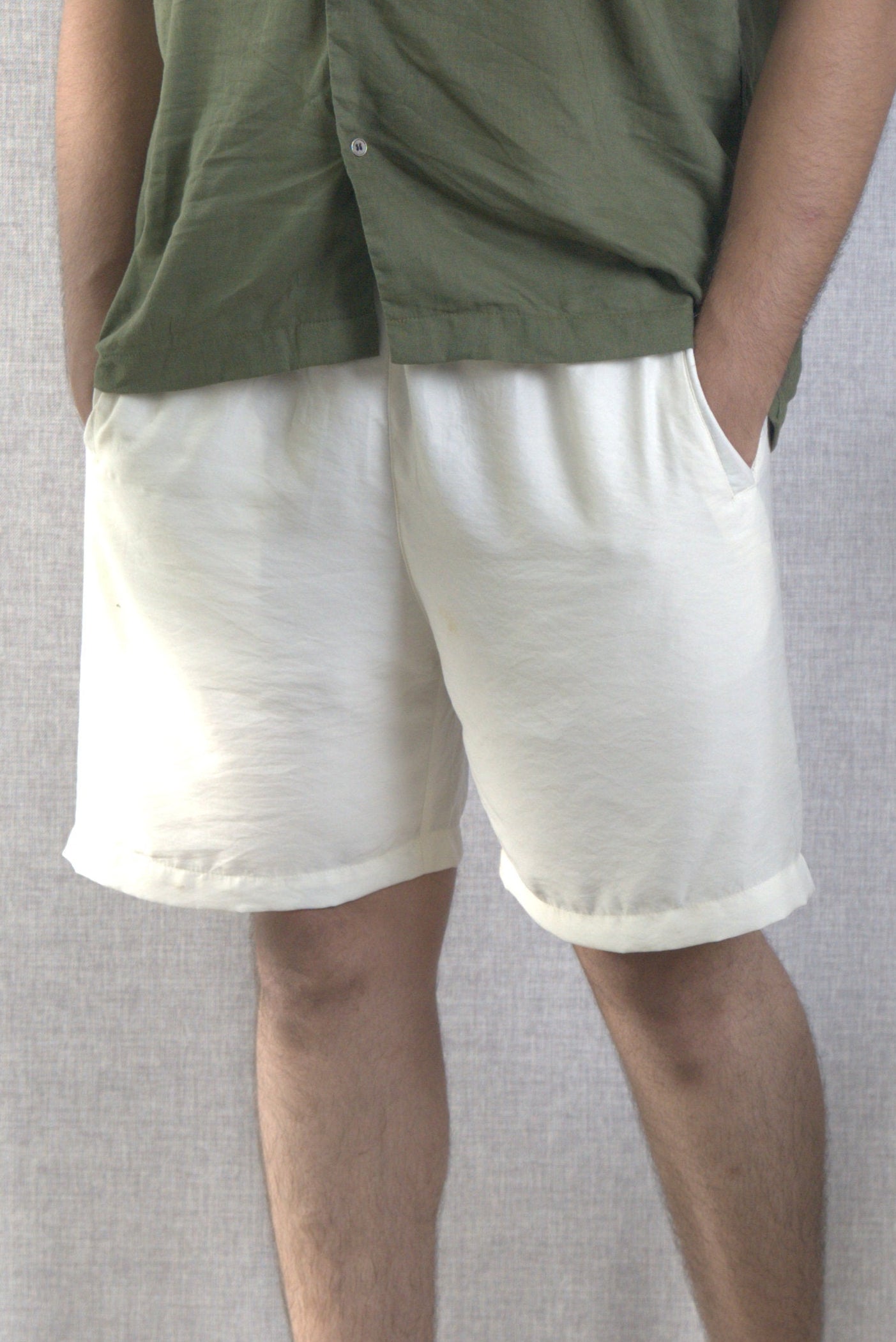 Man wearing a green shirt and white shorts standing in a room with a plant and chair.